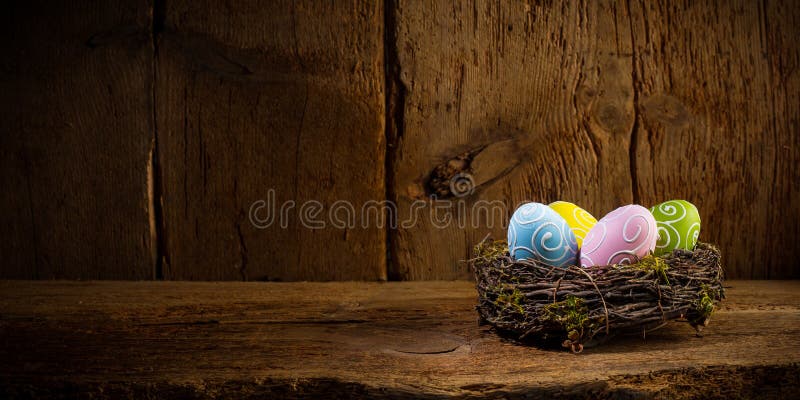 Colorful painted happy easter eggs in birds nest basket on rustic wooden old panorama background copy space