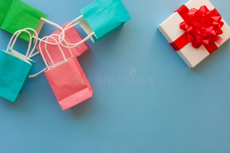 Colorful paper gift bags and white gift box with red bow on blue