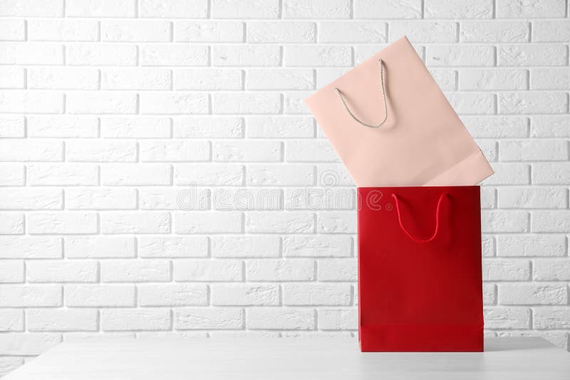 Colorful paper shopping bags on table against brick wall