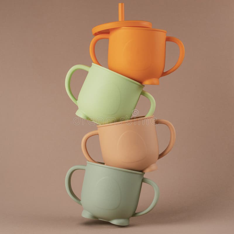 Colorful pastel silicone sippy cups stacked in column on brown background. Baby tableware, feeding concept.