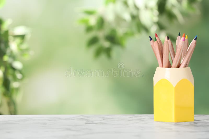Colorful pencils in holder on white marble table. Space for text