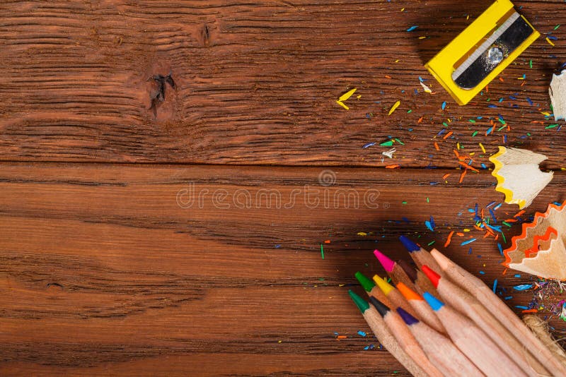 Colorful Pencils with sharpener and shawings on the wood table.