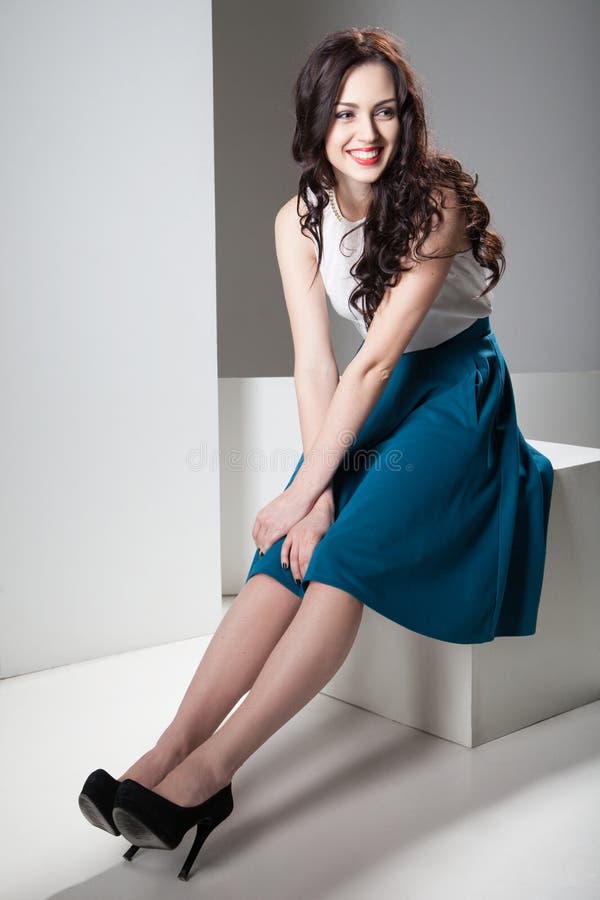 Colorful photo of a woman in white top and dark blue skirt wearing high hells shoes and sitting. Isolated on grey and white background.