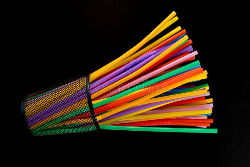 Colorful Plastic Straws Spilling from a Tipped Black Mesh Holder on Black Background stock image