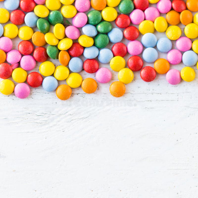 Colorful round candies on white rustic wooden background with c