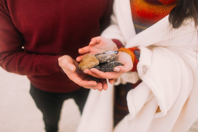 Colorful sea pebbles on couple's hands close up. Happy young couple at the winter beach wrapped in white blanket