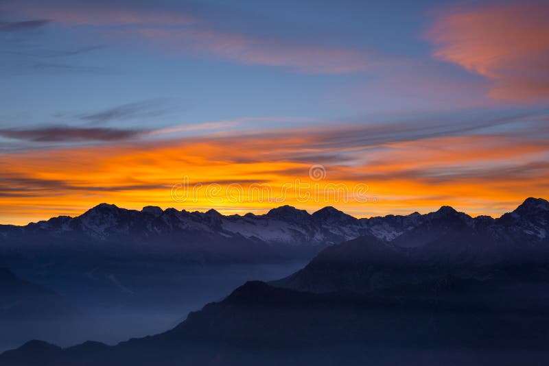 Colorful sunlight behind majestic mountain peaks of the Italian - French Alps, viewed from distant. Fog and mist covering the vall