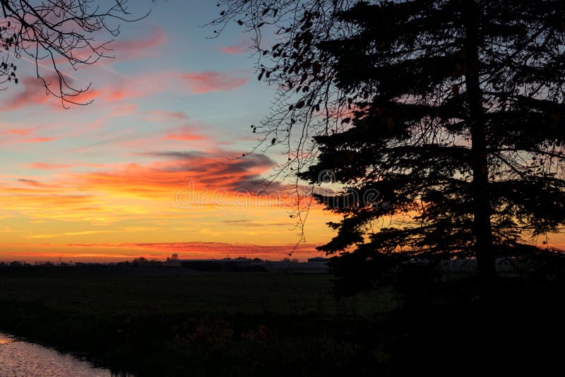 Colorful sunset over the dutch landscape near Gouda, Holland. A tree is silhouetted against the evening sky. stock photo Colorful sunset over the dutch landscape near Gouda, Holland. A tree is silhouetted against the evening sky. stock photo