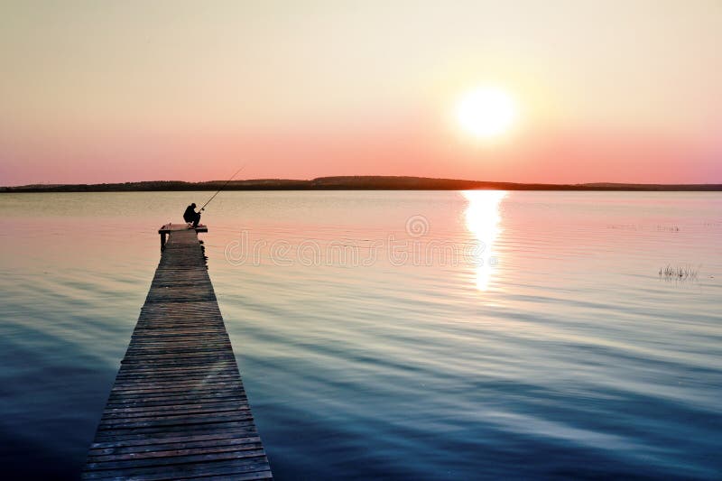 Colorful sunset over the lake with a pier. A lone fisherman is fishing on the pier.