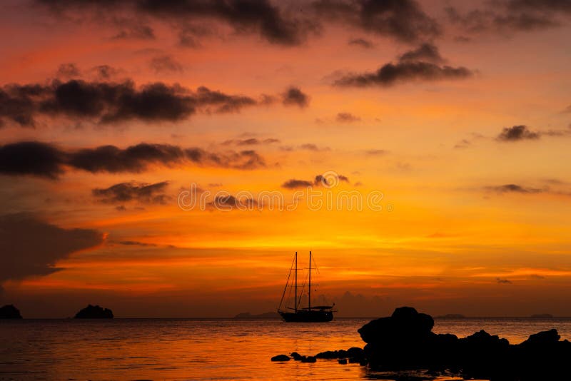 Colorful sunset on a tropical beach. Orange sunset on the ocean. Colorful sunset in the tropics. In the water is a sailing ship.