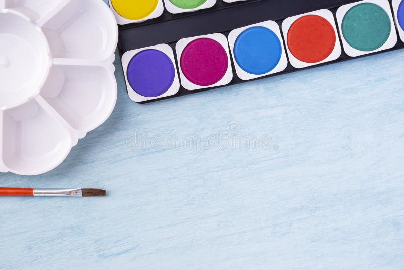 Colorful watercolor tablet with pallette and paint brush on blue texture background