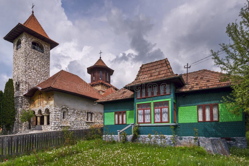 Colorful wooden dwelling and vintage stone and wood Orthodox church with bell tower in the Romanian Carpathian Mountains of