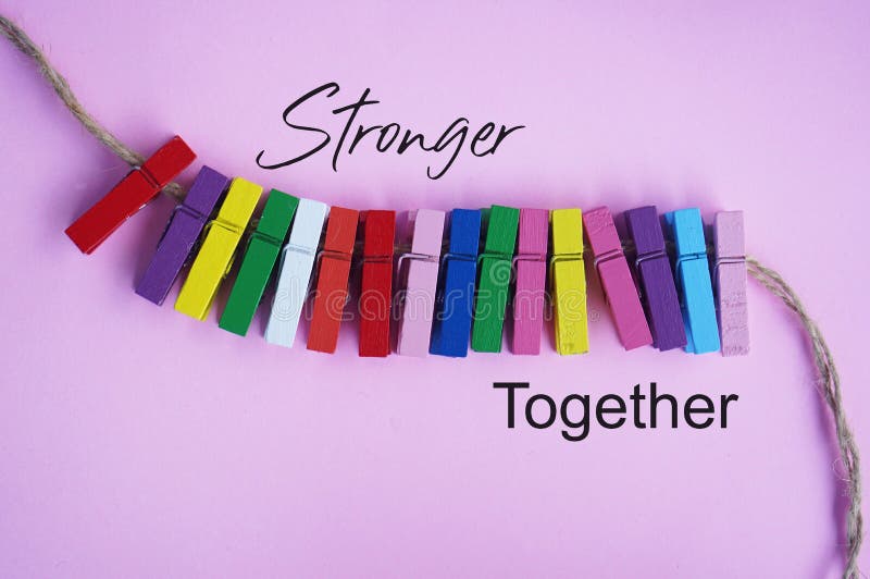 Stronger together. Teamwork and togetherness concept with colorful paper clips attached lined up on pink background.