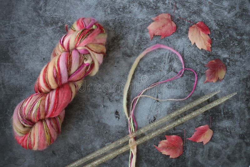 Colorful yarn ball looking like rainbow, two thick needles, segment of yarn like heart and red leaves on grey background stock images Colorful yarn ball looking like rainbow, two thick needles, segment of yarn like heart and red leaves on grey background stock images