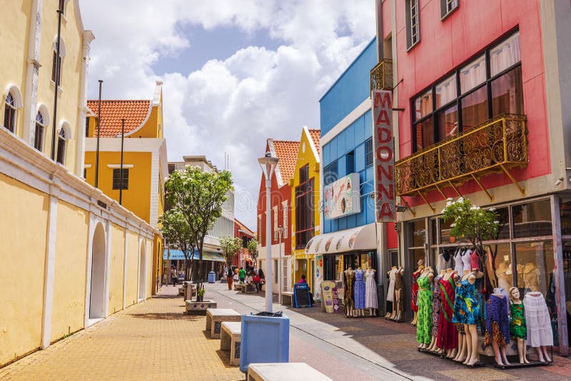Colorida calle caribeña con tienda de ropa maniquíes bancos árboles y edificios coloniales bajo el sol. imagen de archivo