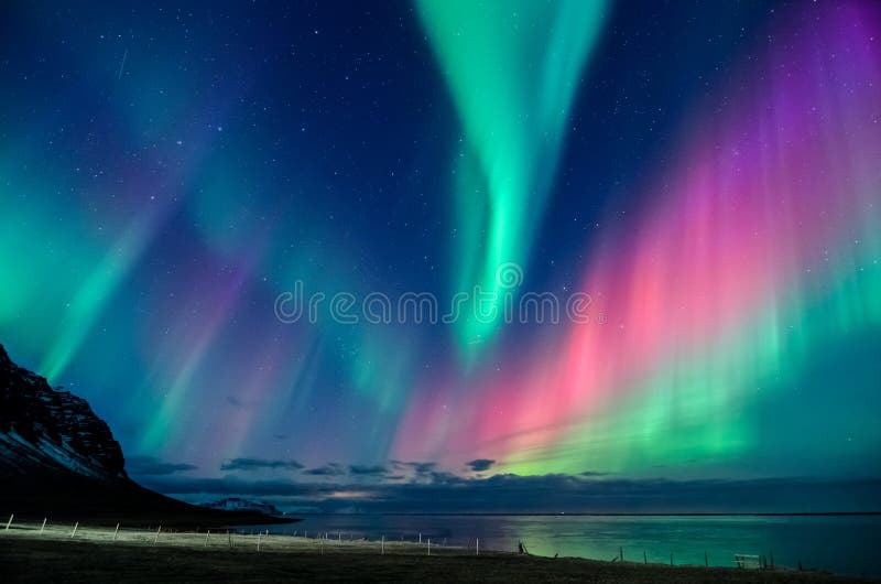 Colorida espiral de luzes setentrionais numa praia da Islândia