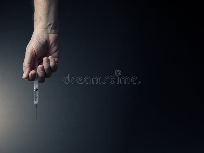 Man`s hand holding syringe with dramatic lighting royalty free stock image
