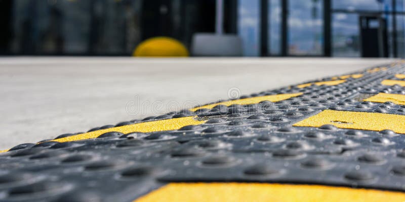 Coloured rubber speed bump located on grey asphalt road against blurred department store building entrance in summer