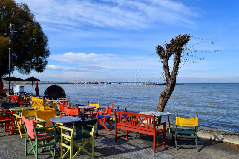 Beautiful cafe on Peraia beach. Colorful chairs and tables in front of blue sea and sky.