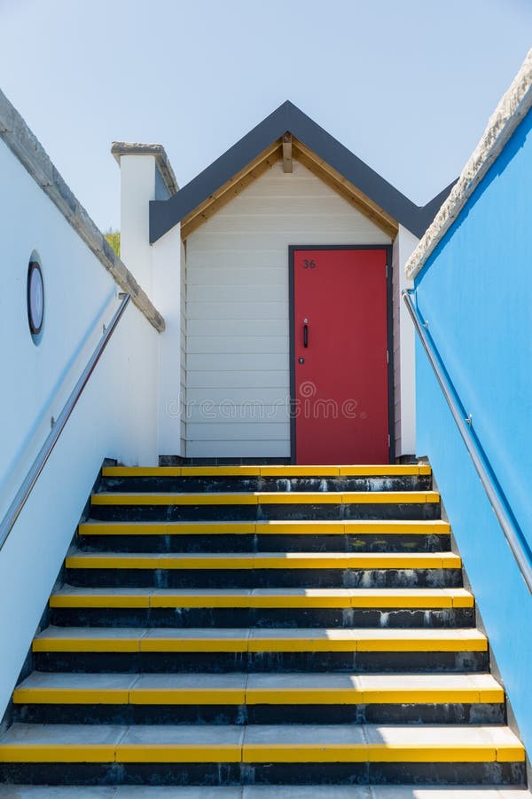 Colourful red door, with each one being numbered individually, of white beach houses on a sunny day, a view looking up the yellow