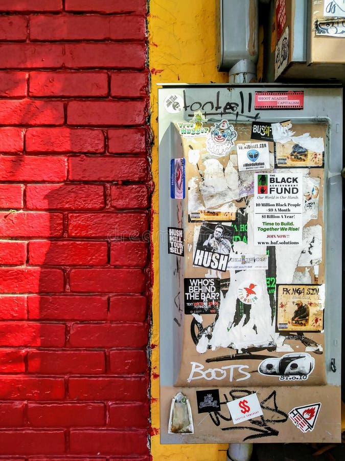 Colorful Urban Brick Building Exterior Wall with Electrical Box and Graffiti Stickers.