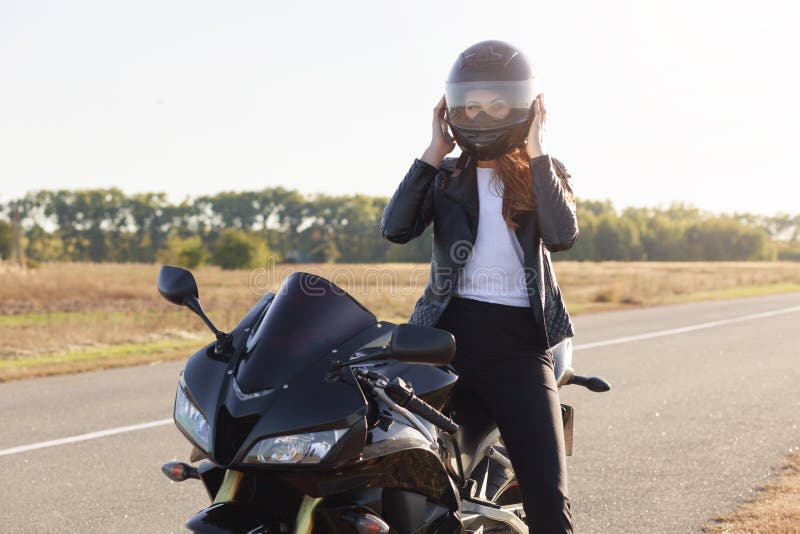 Colpo all'aperto del driver sicuro attraente di moto con il casco che dura per la sicurezza, sedentesi sulla sua motocicletta all fotografie stock Colpo all'aperto del driver sicuro attraente di moto con il casco che dura per la sicurezza, sedentesi sulla sua motocicletta all fotografie stock