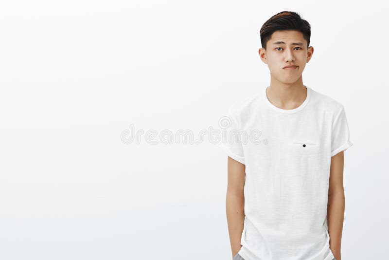 Colpo della vita-su del tipo coreano alla moda bello in maglietta bianca che si tiene per mano nello stare smirking delle tasche immagini stock libere da diritti