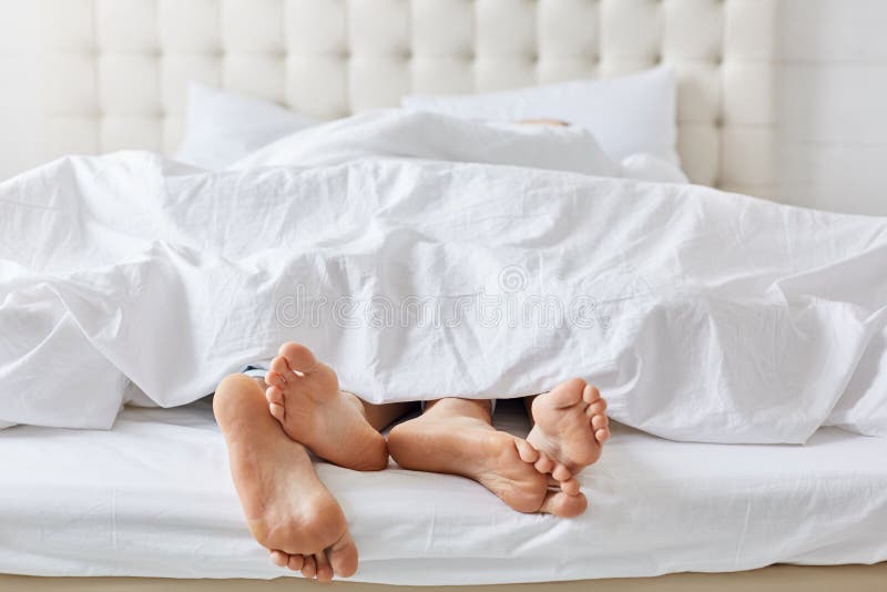 Colpo orizzontale dei piedi delle coppie sotto le coperte da letto bianche a letto alla camera da letto, godendo di buon resto a fotografie stock libere da diritti Colpo orizzontale dei piedi delle coppie sotto le coperte da letto bianche a letto alla camera da letto, godendo di buon resto a fotografie stock libere da diritti