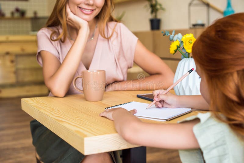 colpo potato di giovane madre sorridente che esamina il piccolo disegno sveglio della figlia con la matita immagini stock libere da diritti colpo potato di giovane madre sorridente che esamina il piccolo disegno sveglio della figlia con la matita immagini stock libere da diritti