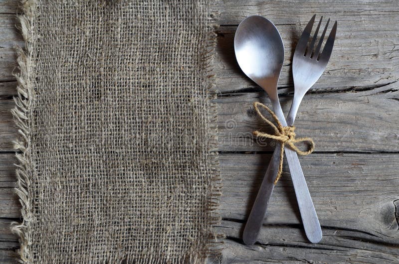 Cutlery set:fork and spoon on burlap cloth on rustic wooden table.Cutlery on old wooden background.Can be used as background menu for restaurant.Selective focus. Cutlery set:fork and spoon on burlap cloth on rustic wooden table.Cutlery on old wooden background.Can be used as background menu for restaurant.Selective focus.