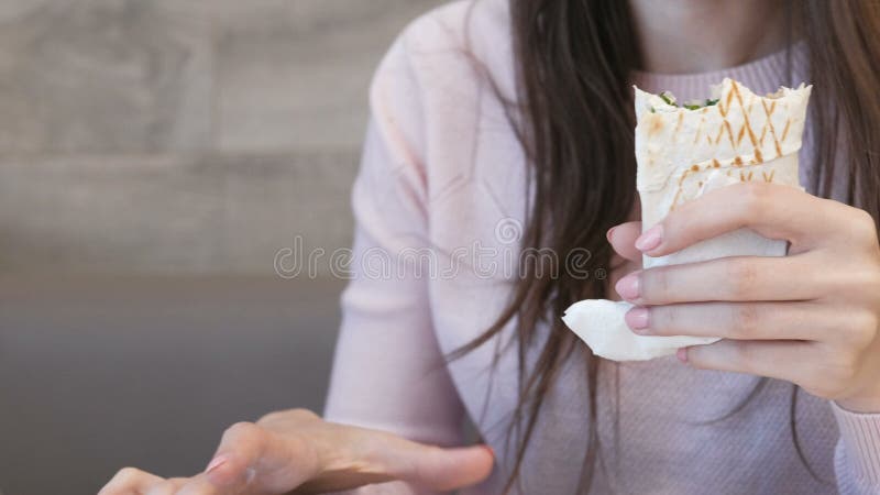 Comer irreconhecível da mulher danar ou Shawarma que senta-se em um café e que datilografa uma mensagem no telefone celular