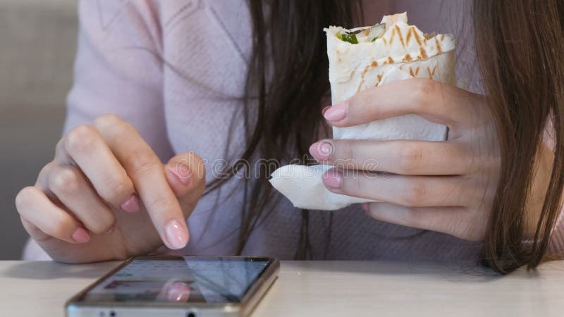 Comer irreconhecível da mulher danar ou Shawarma que senta-se em um café e que datilografa uma mensagem no telefone celular