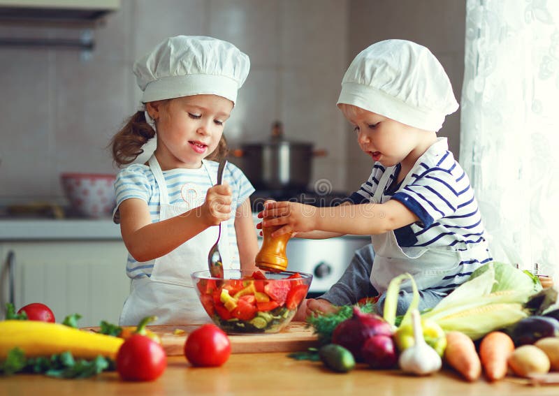 Comer saudável As crianças felizes preparam a salada vegetal no kitc imagem de stock Comer saudável As crianças felizes preparam a salada vegetal no kitc imagem de stock
