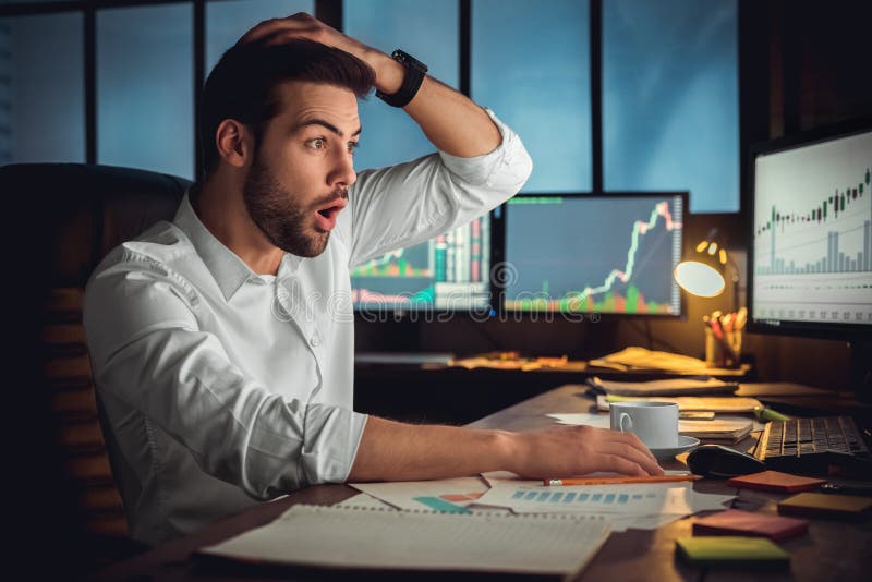 Comerciante de sexo masculino joven en el concepto del trabajo de oficina que se sienta mirando la pantalla chocada fotografía de archivo Comerciante de sexo masculino joven en el concepto del trabajo de oficina que se sienta mirando la pantalla chocada fotografía de archivo