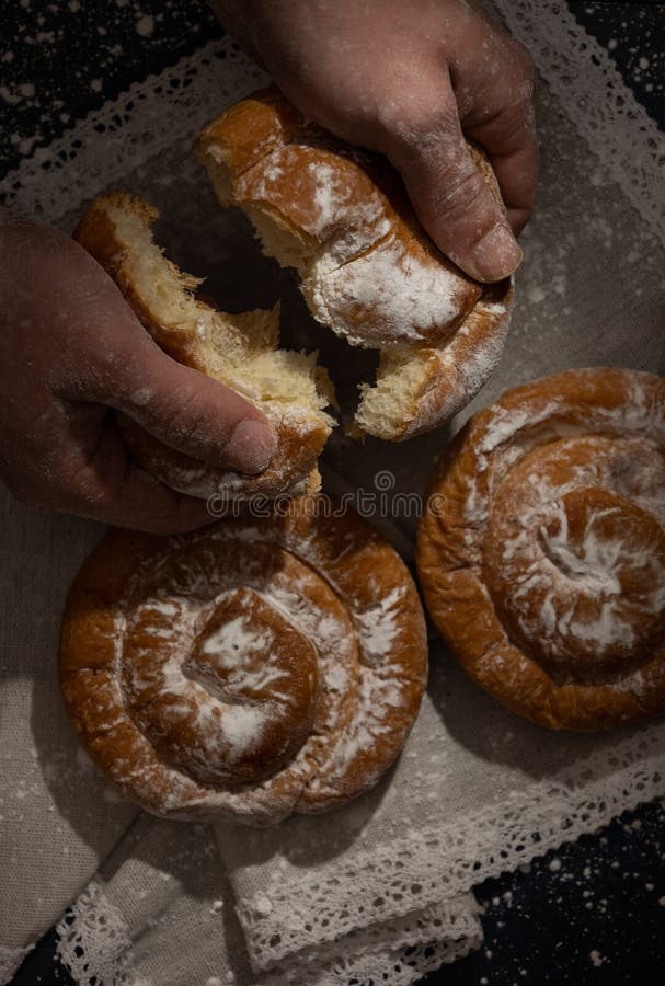 Imagen vertical de una mano de hombre que abre una ensaimada de Mallorca recién horneada en un fondo rústico. Comida oscura. Típica comida mallorquina de España