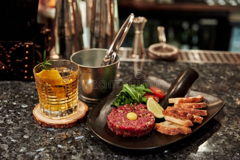 Comida preparada con una pala, tartar de carne, pan blanco, ensalada, un vaso de alcohol fotografía de archivo