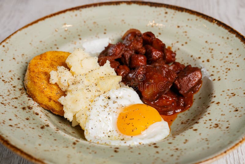 Comida tradicional rumana, polenta con el huevo frito y carne picante imagen de archivo Comida tradicional rumana, polenta con el huevo frito y carne picante imagen de archivo