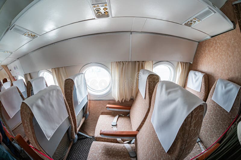 A commercial airplane cabin divided into two sections by curtains. Seats with white headrest covers, emergency exit signs, artificial lighting, and closed overhead compartments are visible. Elegant lighting signs stock images, royalty-free photos and pictures