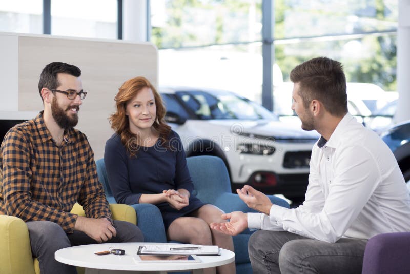 Commerciante di automobile professionista che parla con i compratori in sala d'esposizione esclusiva