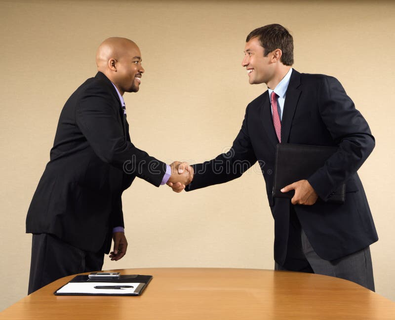Two businessmen in suits shaking hands and smiling. Two businessmen in suits shaking hands and smiling.