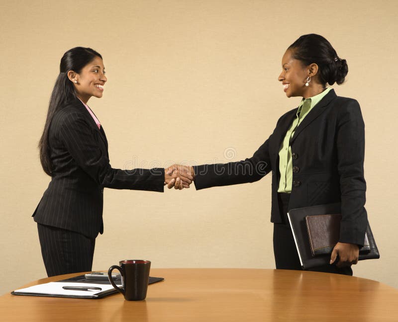 Two businesswomen in suits shaking hands and smiling. Two businesswomen in suits shaking hands and smiling.