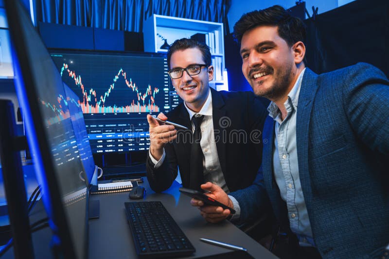 Two stock exchange traders comparing dynamic investment graph via phone and pc with high profit in currency rate. Showing financial benefit data on monitor screen in neon light at workplace. Sellable. Two stock exchange traders comparing dynamic investment graph via phone and pc with high profit in currency rate. Showing financial benefit data on monitor screen in neon light at workplace. Sellable.