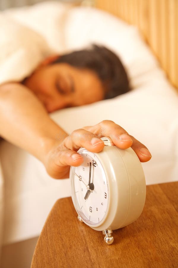 An Indian Asian woman wakes up to turn off a traditional alarm clock. An Indian Asian woman wakes up to turn off a traditional alarm clock