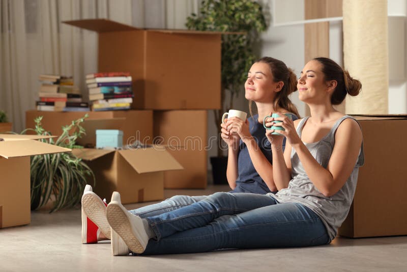 Two happy roommates moving home resting breathing fresh air sitting on the floor in the night. Two happy roommates moving home resting breathing fresh air sitting on the floor in the night