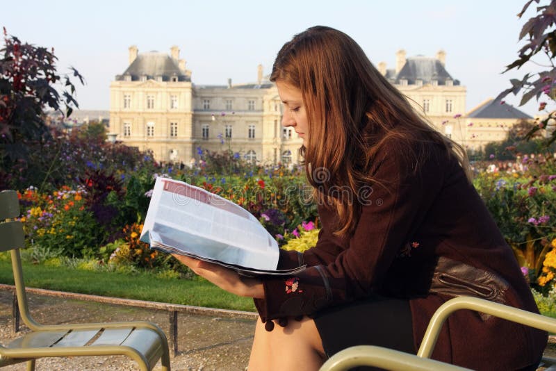 Compartimento bonito da leitura da menina no jardim de Luxembourg (Paris). Sol do fim da tarde. Cores do outono.