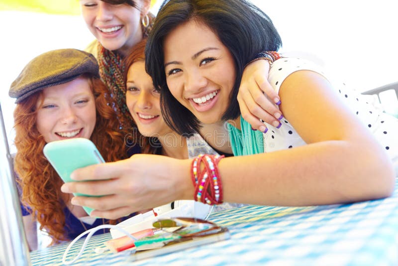 Sharing the latest news. A group of adolescent girls laughing as they look at something on a smartphone screen. Sharing the latest news. A group of adolescent girls laughing as they look at something on a smartphone screen