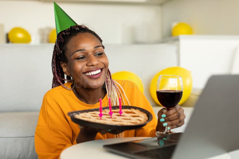 Compleanno online. donna afro-americana felice che festeggia il compleanno con una torta e un bicchiere di vino che parlano al com fotografia stock