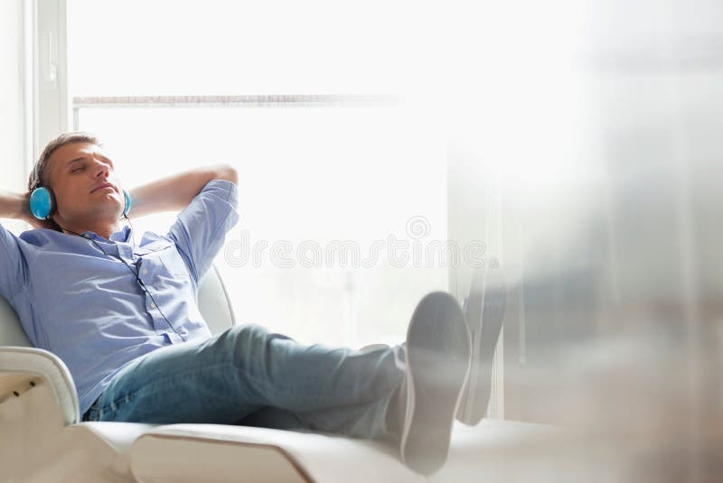 Completo do homem de meia idade relaxado que escuta a música em casa