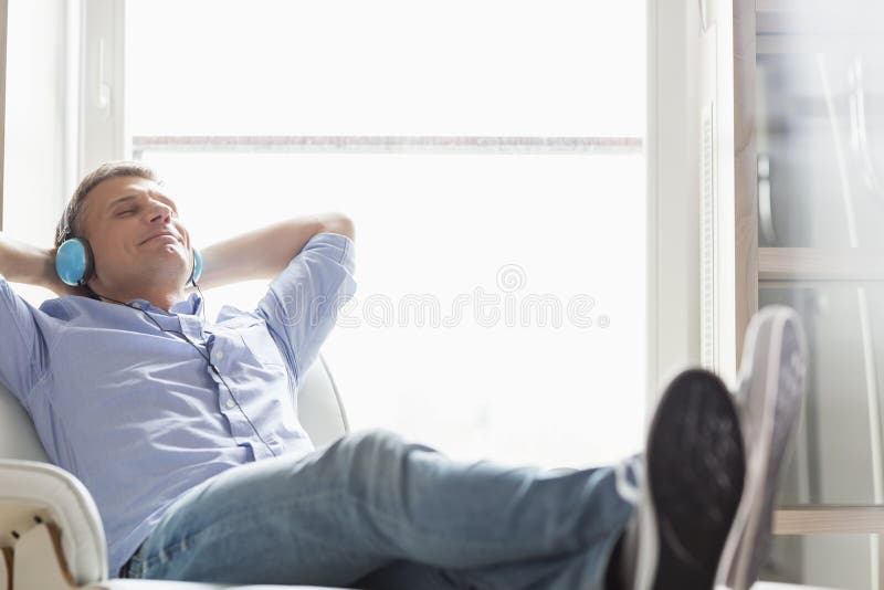Completo do homem de meia idade relaxado que escuta a música em casa
