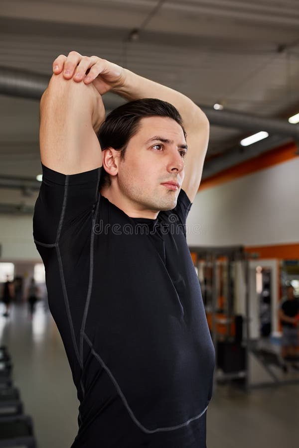 Completo do homem novo no sportswear preto que estica seu braço no gym imagens de stock Completo do homem novo no sportswear preto que estica seu braço no gym imagens de stock